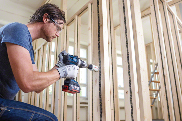 Object #200244880: Bosch_Lochsaege0870 Person wearing safety equipment drills a hole into a wooden stud frame.