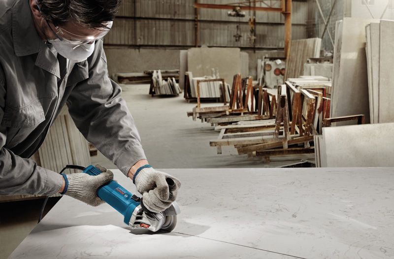 A person wearing safety equipment cuts a large marble slab with a power tool.