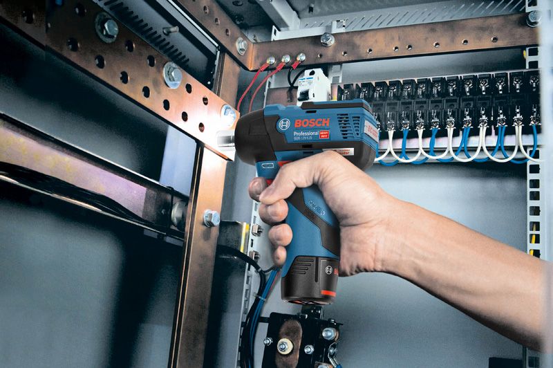 A person uses a cordless impact wrench to fasten bolts inside an electrical panel.