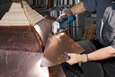 A person wearing safety equipment cuts sheet metal with a cordless metal shear.
