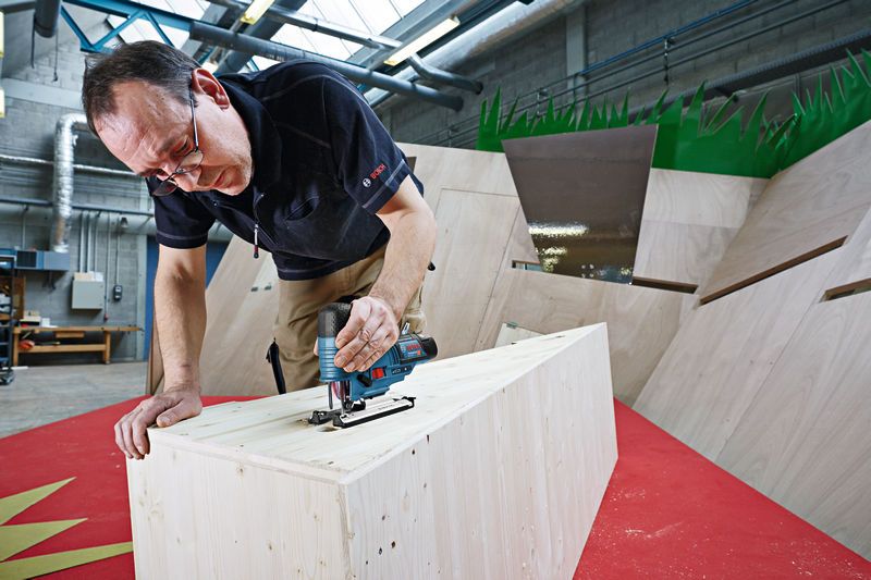 GST 12V-70 A person uses a cordless jigsaw to cut wood in a workshop.