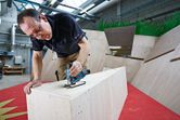 A person uses a cordless jigsaw to cut wood in a workshop.
