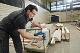 A person wearing safety equipment cuts wood with a cordless jigsaw in a workshop.