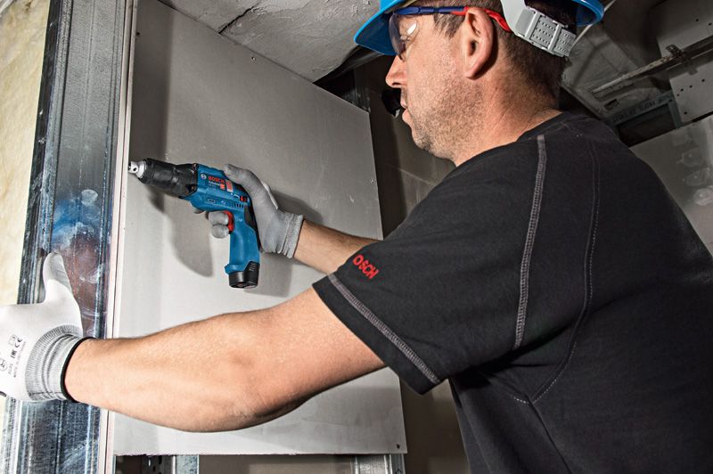 GTB 12V-11 A person wearing safety equipment drives screws into drywall with a cordless screwdriver.