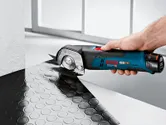 A person uses a cordless universal shear to cut textured rubber flooring.