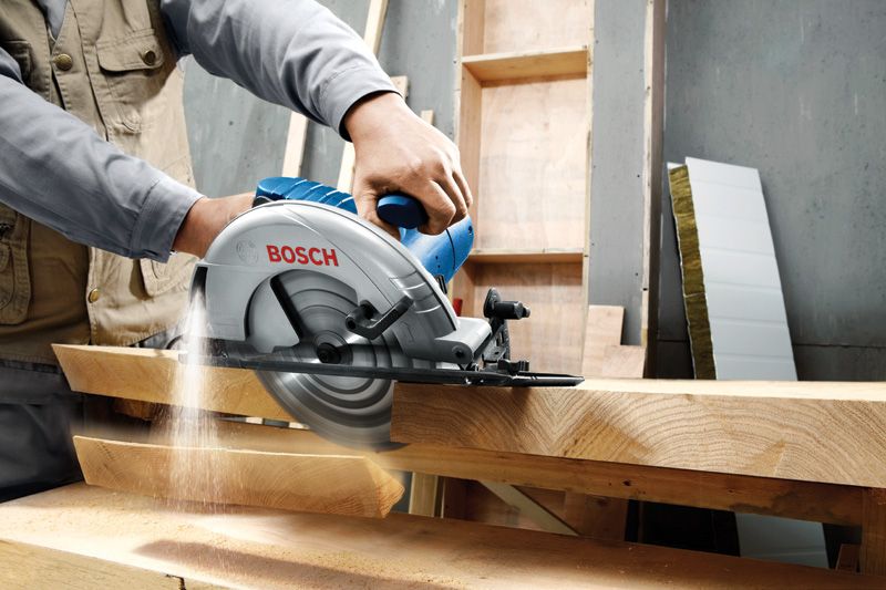 A person guides a circular saw through thick wooden boards in a workshop.