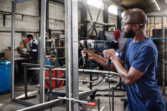HSS Twist Drill Bit PointTeQ 18pcs ToughBox Set 1 - 10 mm Person wearing safety equipment drills into a metal frame in an industrial workshop.