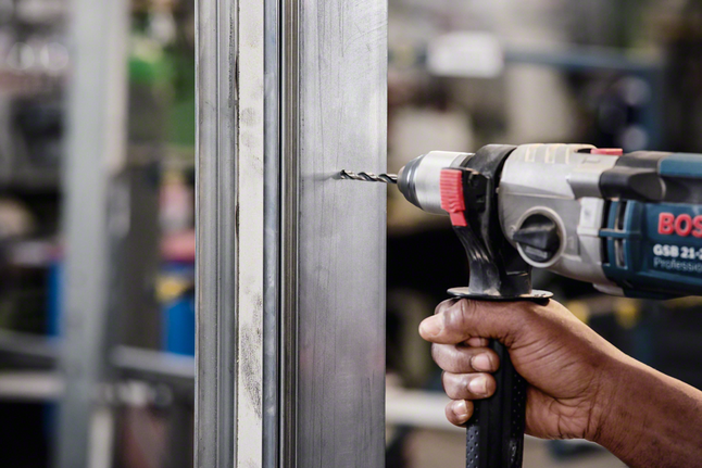 HSS Twist Drill Bit PointTeQ 18pcs ToughBox Set 1 - 10 mm A worker drills a hole through a metal frame indoors.