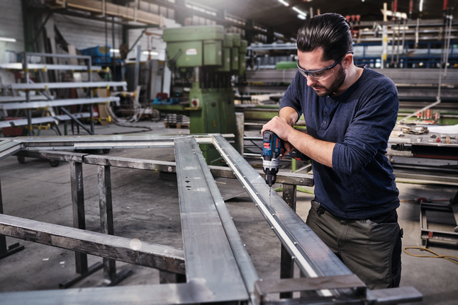 HSS Twist Drill Bit PointTeQ 18pcs ToughBox Set 1 - 10 mm A worker wearing safety equipment drills holes into a metal frame in a factory.