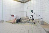 Person installing tiles in a bathroom, using a laser leveling tool on a tripod.