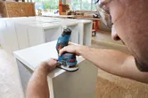 A person wearing safety equipment shapes wood edges using a cordless palm router.