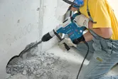 A person wearing safety equipment drills into concrete with a rotary hammer.