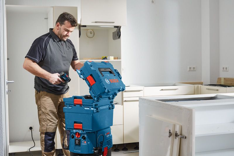 A person opens a blue tool storage box with a drill in a kitchen under renovation.