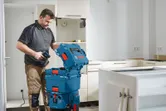 A person opens a blue tool storage box with a drill in a kitchen under renovation.