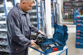 A person in a workshop unpacks a cordless tool set from a hard plastic case.