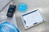 Laser measure on blueprints beside a digital tablet displaying building plans.