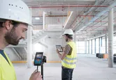 Person wearing safety equipment uses a laser measure in a building under construction.