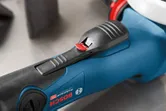 Close-up of a power tool handle with a textured black grip and red safety switch.
