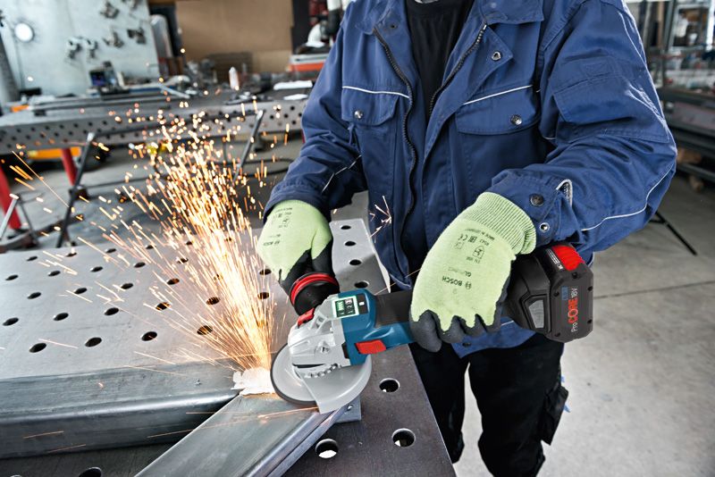 A person wearing safety equipment grinds metal, creating sparks in a workshop.