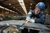 A person wearing safety equipment grinds metal with a power tool in a factory.