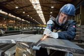 A person wearing safety equipment grinds metal with a power tool in a factory.
