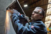 A person wearing safety equipment grinds metal, producing bright sparks.