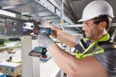 A person wearing safety equipment uses a cordless drill to secure bolts on a steel beam.