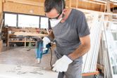 A person wearing safety equipment uses a heat gun to strip paint from a surface.