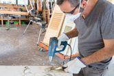 A person wearing safety equipment uses a heat gun to strip paint from wood.