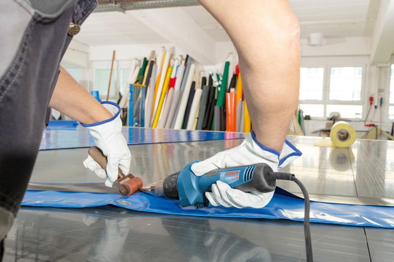 A person wearing safety equipment welds plastic sheeting using a heat gun.