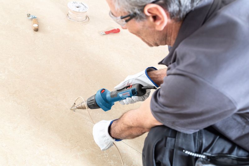 A person wearing safety equipment uses a heat gun to bend plastic tubing on the floor.