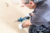 Person wearing safety equipment uses a heat gun to bend plastic tubing on a floor.