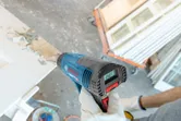 A person wearing safety equipment uses a heat gun to strip paint from a door.