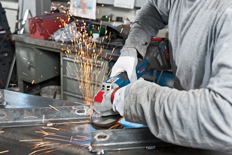 A person wearing safety equipment uses an angle grinder to cut metal, creating sparks.