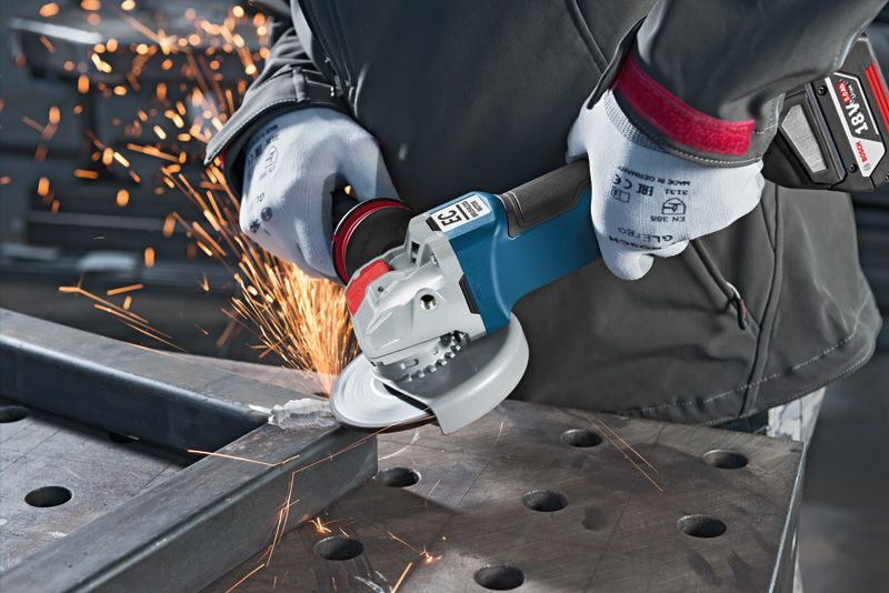 A person wearing safety equipment grinds metal with a cordless angle grinder, sparks flying.