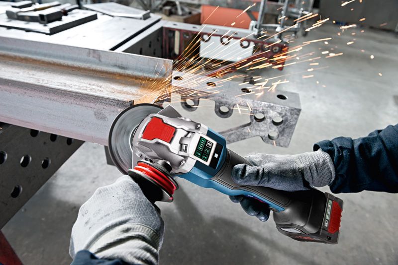 A person wearing safety equipment grinds metal with a cordless angle grinder, producing sparks.