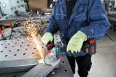 A person wearing safety equipment uses an angle grinder to cut metal, creating sparks.