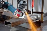 A person wearing safety equipment grinds metal with an angle grinder, sending out sparks.