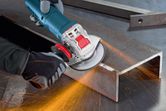 A person wearing safety equipment grinds a metal beam with an angle grinder.