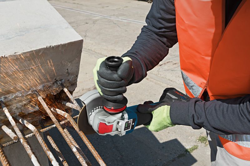 A person wearing safety equipment cuts rebar with a cordless angle grinder.