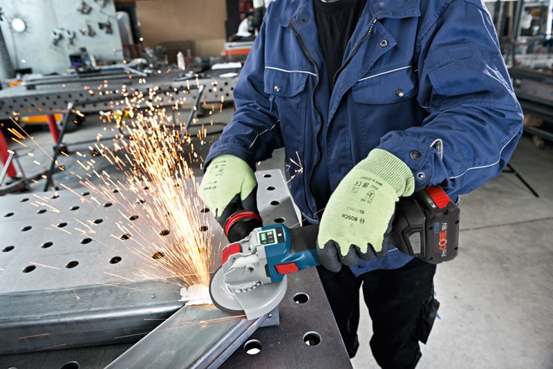 A person wearing safety equipment grinds metal with a cordless angle grinder.