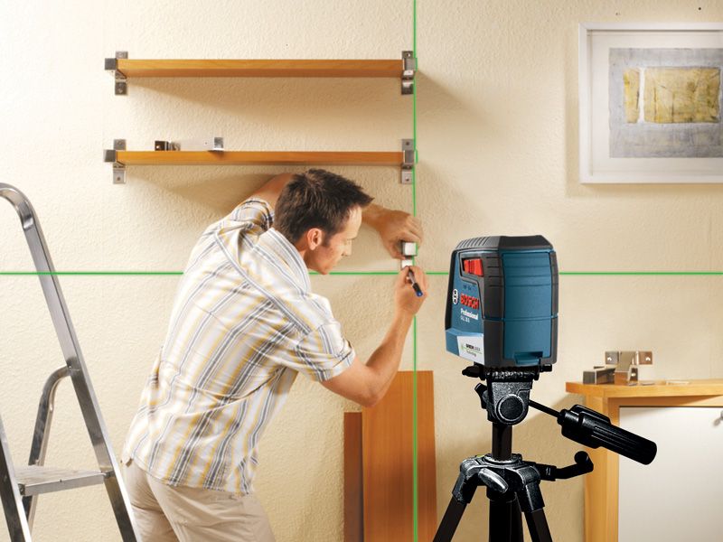 A person marks a wall for shelving using a green laser leveling tool.