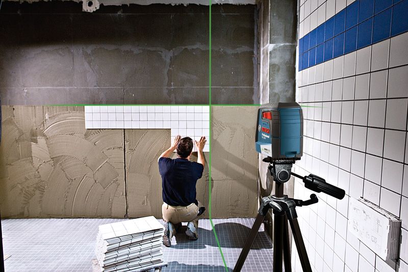 Person installs wall tiles using a laser leveling tool to align rows.
