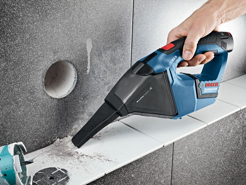 Person uses a cordless vacuum cleaner to remove dust from a tiled surface.