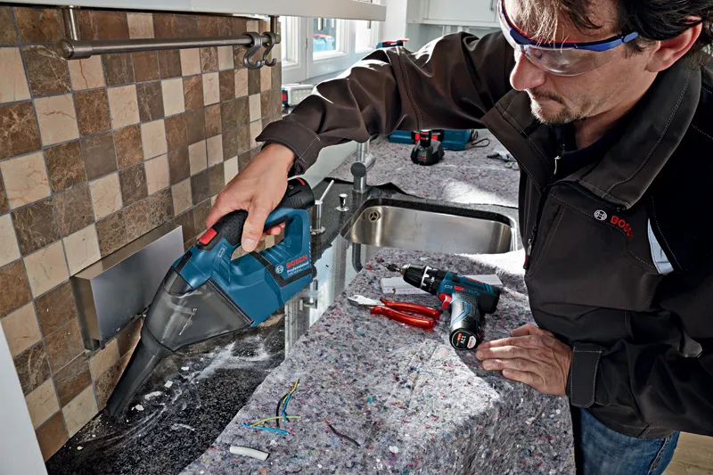 Person wearing safety equipment cleans construction debris with a cordless vacuum cleaner.