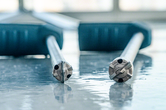 Two drill bits with blue handles rest on a reflective surface.