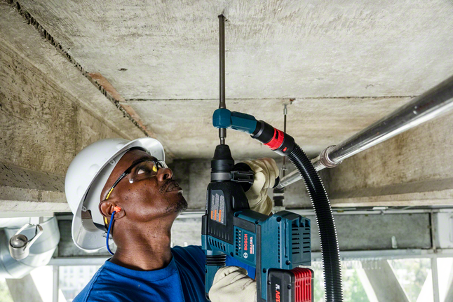 Person wearing safety equipment drills into a concrete ceiling with a rotary hammer.