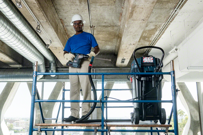 A person wearing safety equipment operates a power tool on scaffolding.