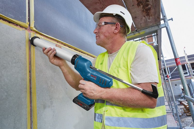 GCG 18V-600 A person wearing safety equipment applies sealant to a wall joint with a cordless caulk gun.