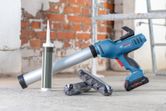 Cordless caulk gun on a concrete floor beside caulk cartridges in a construction area.